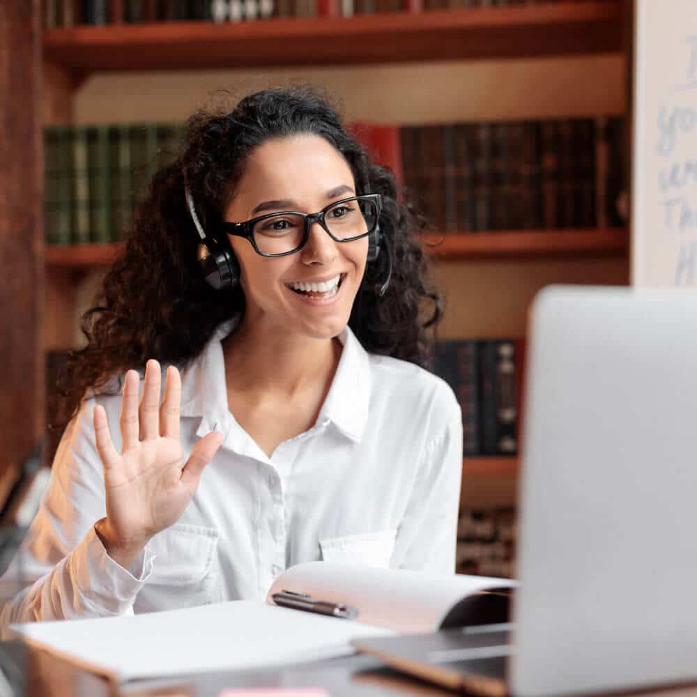 Woman attending an online meeting, waving hello toward the screen